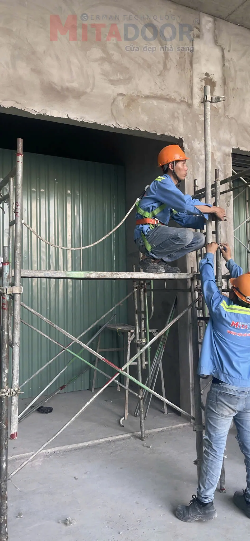 Thợ lắp đặt cửa cuốn Mitadoor đeo dây an toàn trên giàn giáo cao, đảm bảo an toàn lao động trên cao.